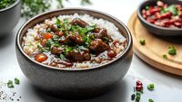 Hearty beef stew served over steamed white rice in dark ceramic bowl, garnished with fresh herbs and accompanied by chili peppers, comfort food styling.