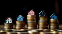 Small houses placed on stacks of gold coins showing real estate market growth and property investment concept against dark background with selective focus.