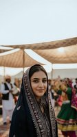 Young South Asian woman in traditional embroidered dupatta at cultural festival celebration with colorful crowd under tent canopy for wedding events.