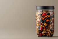 Glass jar filled with colorful dried fruits, nuts and berries mix for healthy snacking and cooking ingredients on neutral background.