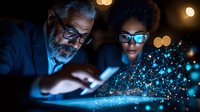 Mature Asian businessman and African American woman analyzing digital transformation with glowing particles from tablet in dark office environment.