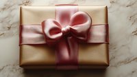 Elegant gift box wrapped in metallic gold paper with luxurious pink satin ribbon and bow on marble surface, perfect for special occasions and celebrations.