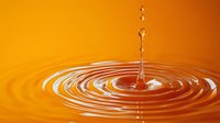 Water drop falling into orange liquid creating concentric ripple circles with splash droplets against vibrant warm background, macro photography.