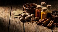 Aromatic spices and essential oils arranged on rustic wooden table with cinnamon sticks, star anise, walnuts and glass bottles for natural wellness.