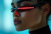 Young Asian woman wearing futuristic LED glasses with red light effect against cyan background, profile view showing defined facial features and black turtleneck.