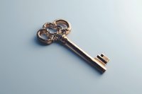 Vintage ornate golden key with decorative bow handle and intricate baroque details on light blue background, isolated macro shot for design projects.