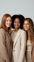 Three diverse professional women in beige business suits smiling together, representing teamwork, corporate success and workplace diversity in modern office.
