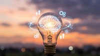 Young male entrepreneur with light skin tone holding glowing lightbulb containing brain and digital icons against sunset sky. Represents innovation, creativity, business strategy and problem-solving for corporate presentations and educational content.