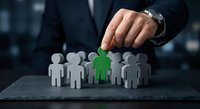 Businessman hand selecting green figure from group of people icons on dark surface representing talent acquisition and human resources recruitment strategy.