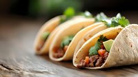 Mexican street tacos with seasoned meat, fresh cilantro, and diced tomatoes served on rustic wooden surface, selective focus on foreground taco creates appetizing depth.
