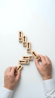 Businessman hands arranging wooden blocks with arrows and target symbols showing step-by-step growth strategy and goal achievement process.