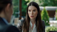 Young Caucasian businesswoman in grey suit jacket and white blouse listening attentively during outdoor meeting, natural bokeh background, professional portrait.