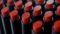 Red lipsticks in black tubes arranged in rows creating dramatic pattern with selective focus. Cosmetic and beauty industry concept showing luxury makeup products.