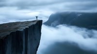 Silhouette of person standing with raised arms on Preikestolen cliff edge above misty fjord in Norway, dramatic mountain landscape in foggy weather.