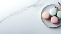 Pastel pink and mint macarons on gray ceramic plate against white marble background with lavender sprig, flat lay composition with copy space.