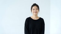 Young Asian woman in black sweater smiling warmly at camera against white background. Professional portrait for business, lifestyle content.