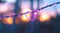 Glowing pink heart-shaped light on string lights against blurred bokeh background creates romantic mood for Valentine's Day or wedding decor.