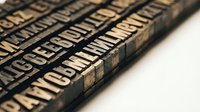 Vintage wooden letterpress type blocks with raised letters arranged in rows, showcasing traditional printing craftsmanship and typography history.