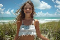 Young woman in white crochet crop top enjoying summer beach day, wind blowing through hair, natural beauty against turquoise ocean and blue sky background, perfect for lifestyle and travel content.