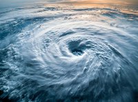 Aerial view of massive hurricane eye over ocean waters with dramatic spiral cloud formations and stormy atmosphere during sunrise or sunset. Natural disaster concept.