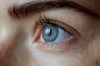 Close-up macro shot of bright blue eye with long eyelashes and natural freckles on fair skin, showing intricate iris detail in soft natural lighting.