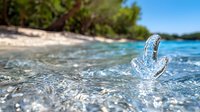 Crystal clear glass anchor floating on turquoise ocean waves near tropical beach with white sand and green palm trees, summer vacation concept.