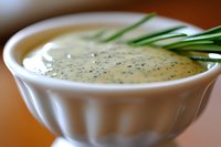 Creamy ranch dressing with fresh chives in white ceramic bowl, shallow depth of field focus on herbs and sauce surface, macro food photography.