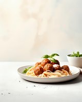 Homemade spaghetti with meatballs garnished with fresh basil on ceramic plate against neutral background, classic Italian cuisine.