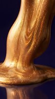 Cropped view of female leg and foot coated in shimmering gold glitter against dark blue background, showcasing luxurious metallic body art for cosmetics and beauty campaigns.