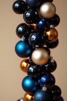 Festive arrangement of shiny Christmas baubles in black, gold, silver and blue creating elegant holiday decoration against neutral background.
