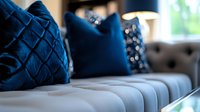 Elegant gray tufted sofa with luxurious navy blue velvet decorative pillows featuring diamond pattern and geometric designs in modern living room interior.