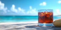 Refreshing cocktail with ice cubes in glass on wooden surface against blurred tropical beach background with turquoise ocean water and blue sky.