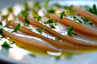 Fresh raw fish slices garnished with herbs and olive oil on white plate, macro shot with selective focus. Elegant presentation for restaurant menu.