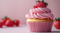 Pink frosted vanilla cupcake topped with fresh strawberry in pink paper liner against soft pink background with scattered berries, macro food photography.