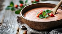 Fresh strawberry gazpacho garnished with mint leaves and berries in rustic ceramic bowl on wooden background. Cold summer soup for healthy eating.