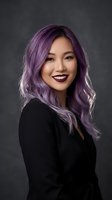 Young Asian woman with vibrant purple hair and dark lipstick smiling confidently in black outfit against gray studio background for beauty and fashion concepts.
