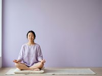 Young Asian woman in lotus position meditating on yoga mat against purple wall. Mindfulness and wellness practice for relaxation and mental health.