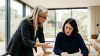 Two professional businesswomen collaborating in modern office space with large windows and natural lighting for corporate teamwork presentations.