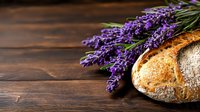 Fresh artisan bread loaf with fragrant lavender flowers on rustic wooden background, creating contrast between baked goods and aromatic herbs.