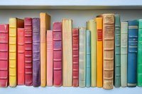 Colorful vintage hardcover books arranged in a row on white shelf, showcasing various sizes and binding styles in red, yellow, blue, and green tones.