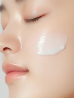 Close-up of young woman applying white moisturizing cream on face with closed eyes showing skincare routine and beauty treatment for healthy skin.