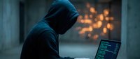 Hooded hacker in dark environment working on laptop with glowing code on screen. Cybersecurity threat concept for digital security and data protection awareness.