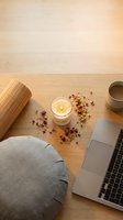 Cozy workspace with laptop, candle, dried flowers and cushion on wooden desk creating warm atmosphere for remote work and relaxation.