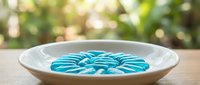 Blue spiral pasta shells arranged in white ceramic bowl on wooden table with blurred green garden background for cooking and food photography.