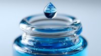 Crystal clear water droplet suspended above blue liquid surface with ripples, showcasing fluid dynamics and surface tension in macro photography.