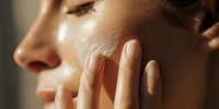 Close-up profile of woman with glowing skin touching face in warm sunlight, showcasing skincare routine and natural beauty.