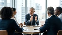 Mature male executive with gray hair leading business meeting with diverse colleagues in modern office with city skyline view, discussing strategy and collaboration.