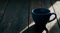 Empty dark navy ceramic mug with handle on wooden surface casting shadow, suitable for beverage mockups and lifestyle designs.