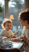 Young mother and toddler sharing breakfast at home, wearing matching cream sweaters, with winter morning light streaming through window.