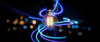 Vintage Edison bulb with glowing blue and green light trails swirling around against dark background with bokeh lights for creative energy concepts.